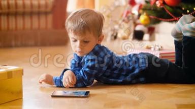 可爱的小男孩躺在圣诞树旁边的地板上，在智能手机上看动画片的4k视频。 <strong>好孩子</strong>